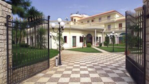 A large, multi-story building with a checkered tile entrance, stone walls, and a well-maintained lawn. - Parco Serrone (Corato)