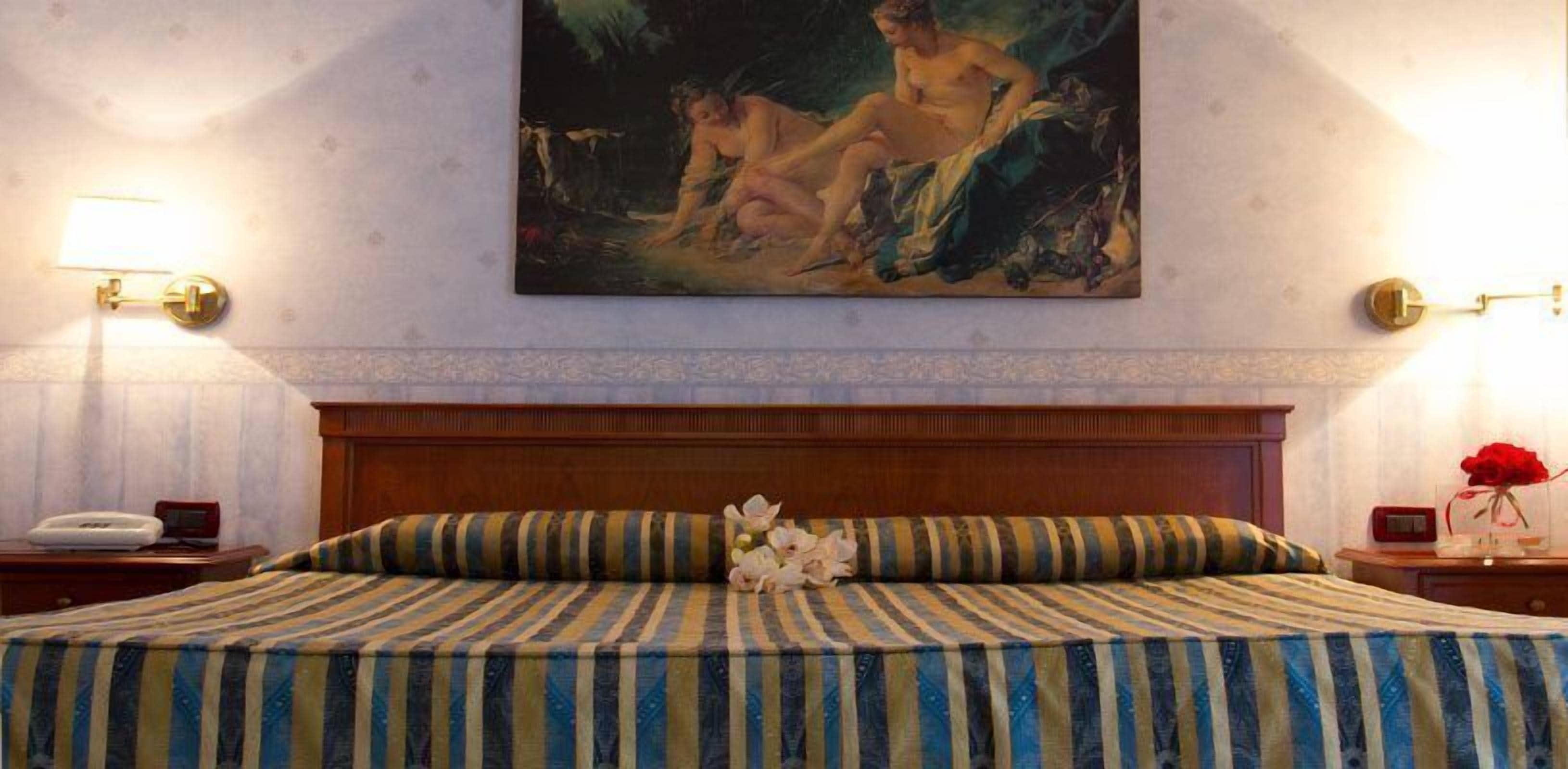 Ein Hotelzimmer mit einem großen Bett, einem Gemälde darüber und zwei Nachttischen mit Lampen.