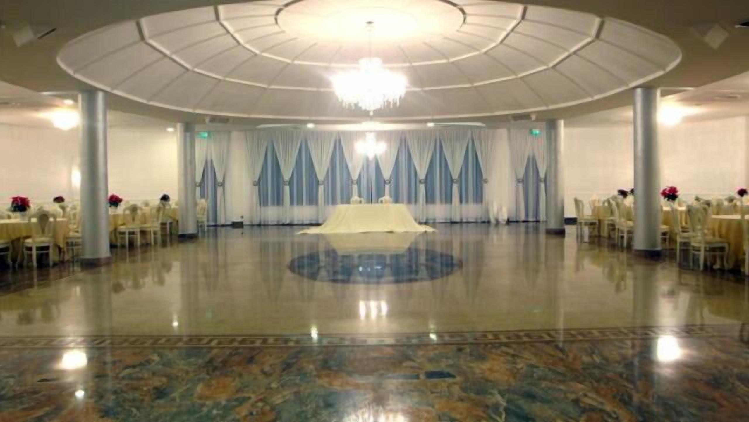 Un salón amplio y circular, con piso pulido, mesas y sillas blancas dispuestas para un evento.
