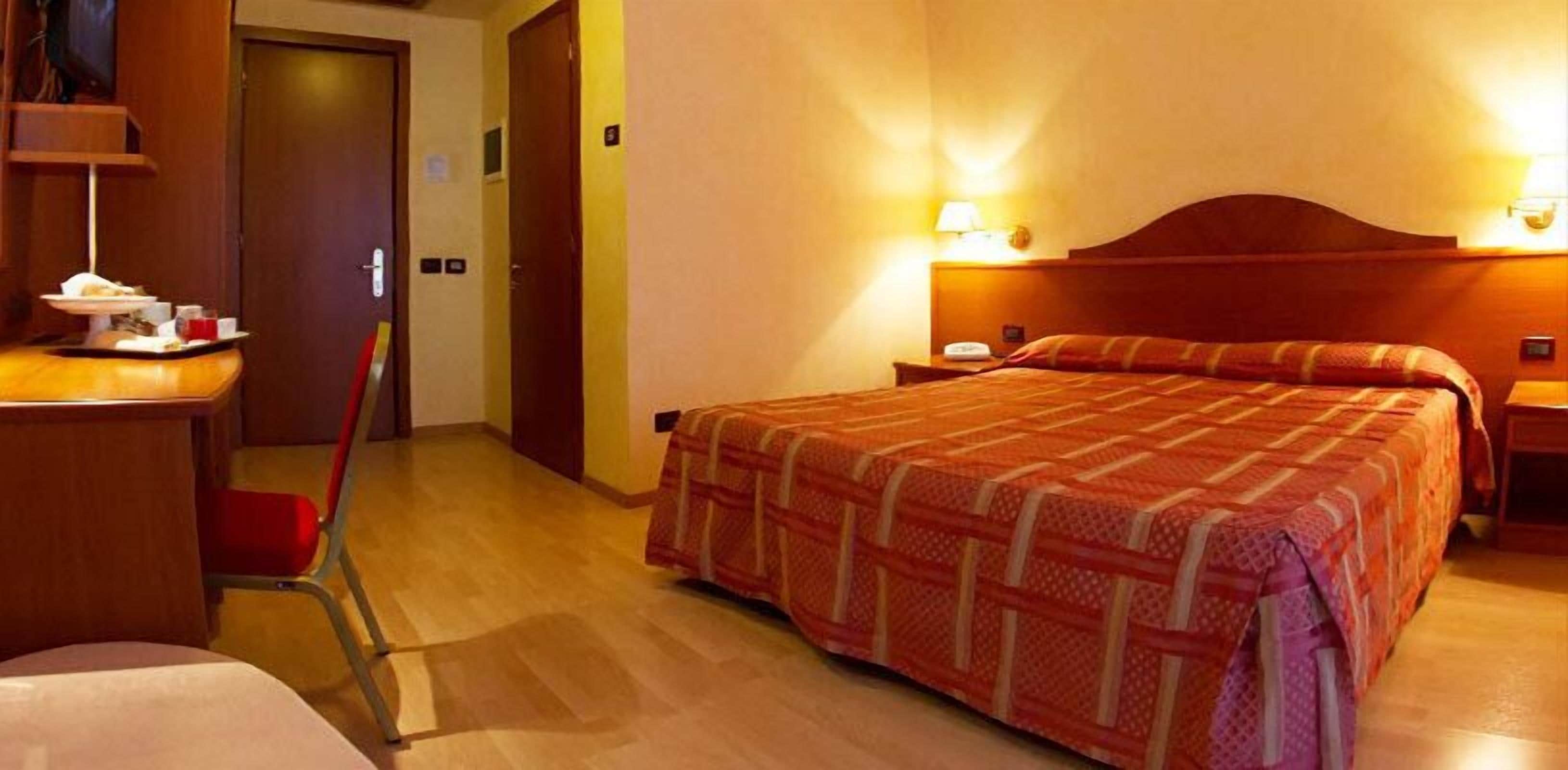 Ein Hotelzimmer mit Bett, Nachttischen, einem Schreibtisch und einem Stuhl sowie einer Tür.