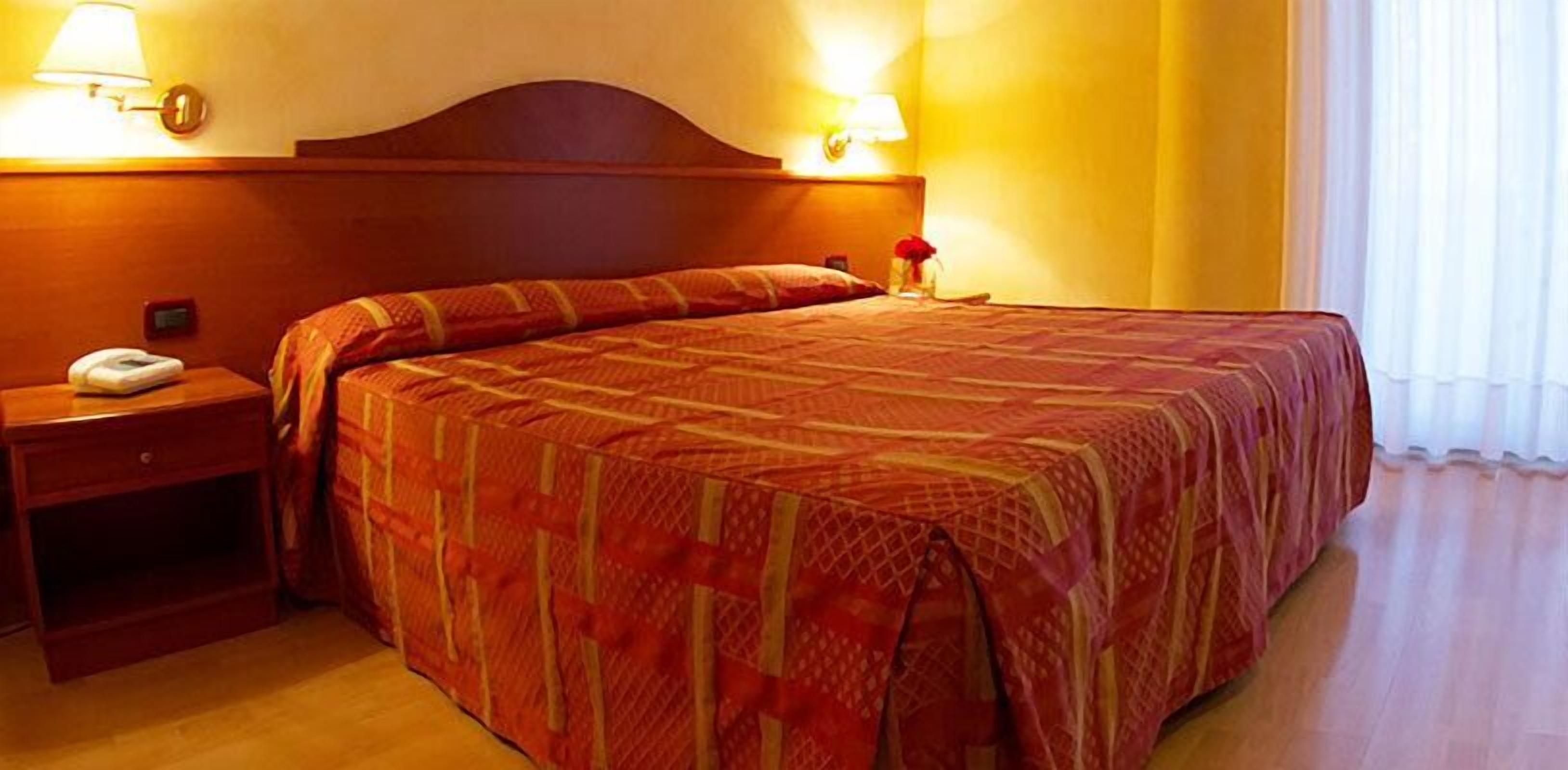A hotel room with a large bed, a nightstand with a phone, and two wall-mounted lamps.
