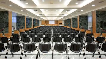 A conference room with rows of chairs, a podium, and a large screen at the front.