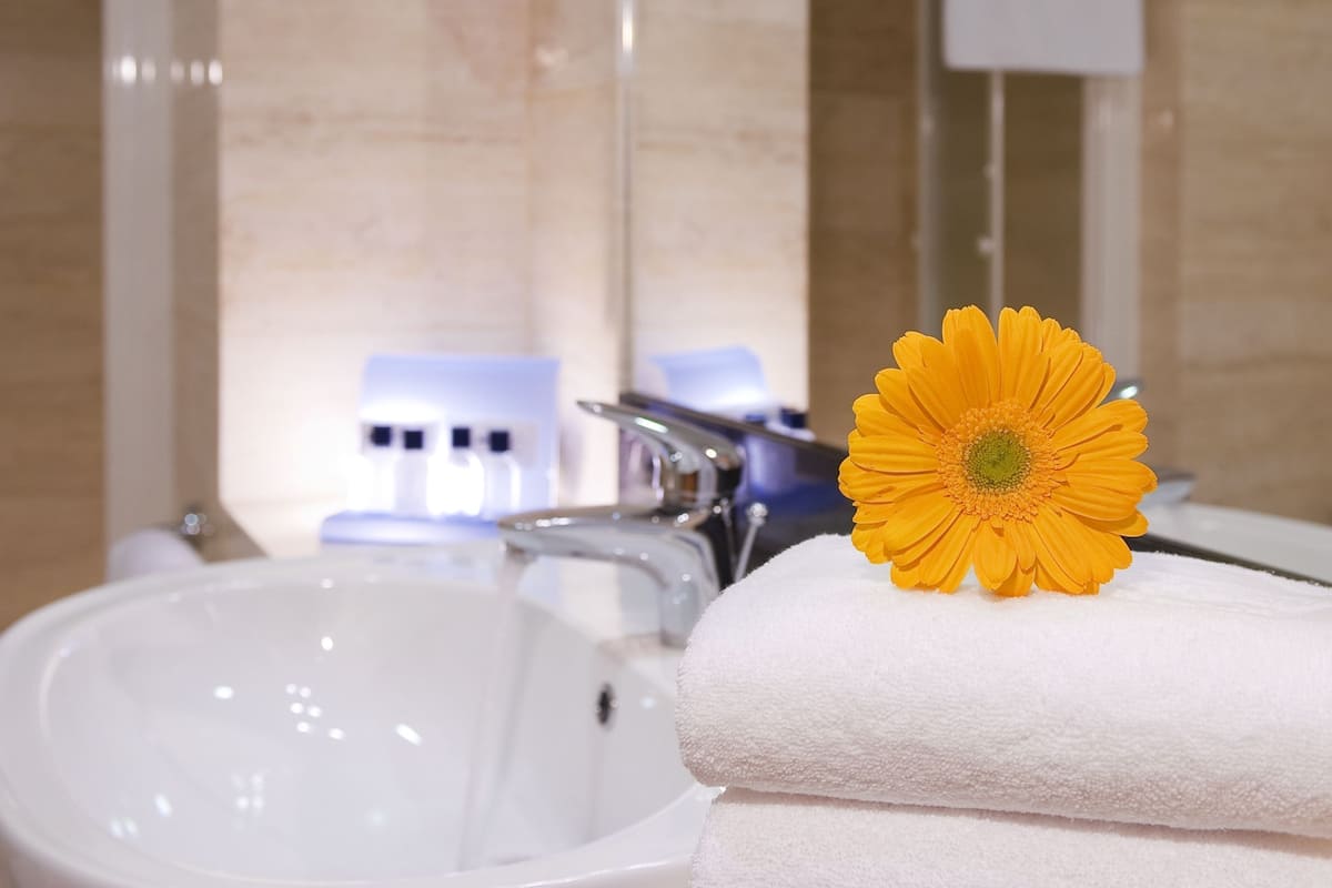 Un baño con lavabo, espejo, toallero y una flor.