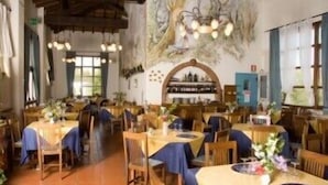 A restaurant with multiple wooden tables and chairs, a rustic ceiling, and a decorative wall with a tree mural. - Hotel Residence Sant'Uberto (Roccastrada)