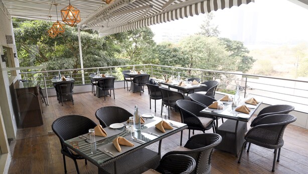 An outdoor dining area with multiple tables and chairs, surrounded by a railing, overlooking a lush green landscape.