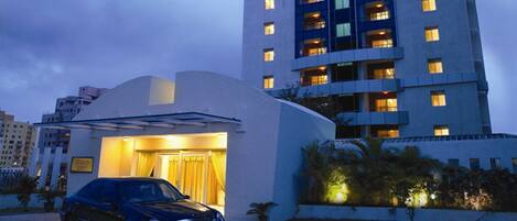 A modern hotel with a curved facade, a car parked in front, and a well-lit entrance.