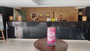 A reception area with a black counter, two receptionists, framed certificates on the wall, and a decorative vase with pink flowers on a round table.