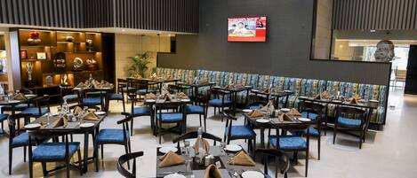 Un grand espace dédié à la salle à manger, avec plusieurs tables et chaises, un téléviseur fixé au mur et un élément décoratif mural.