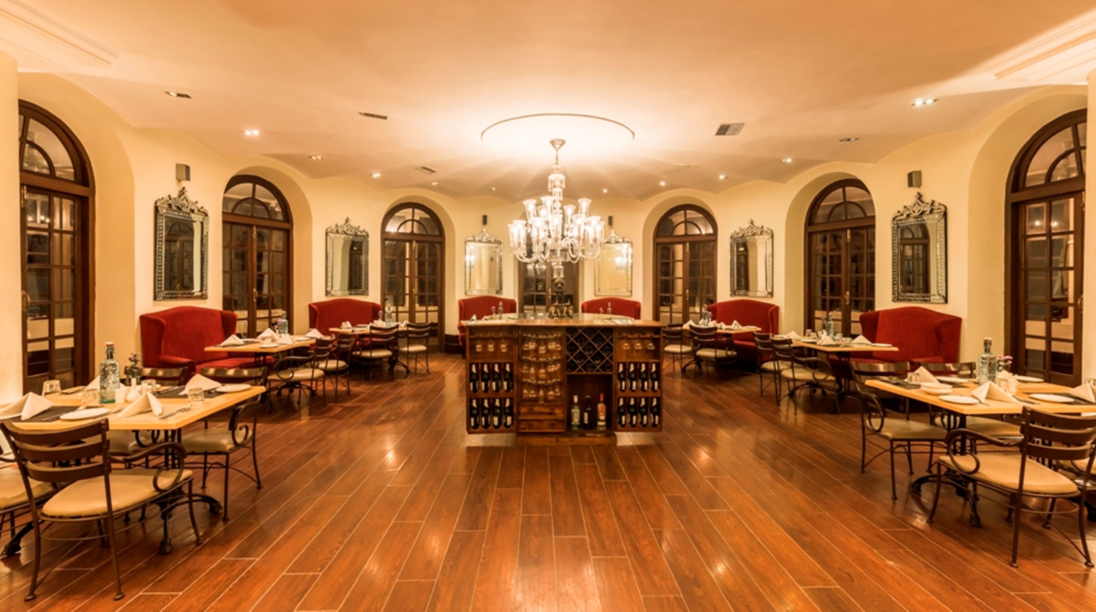 A spacious dining area with wooden flooring, red upholstered chairs, and a central wine rack.