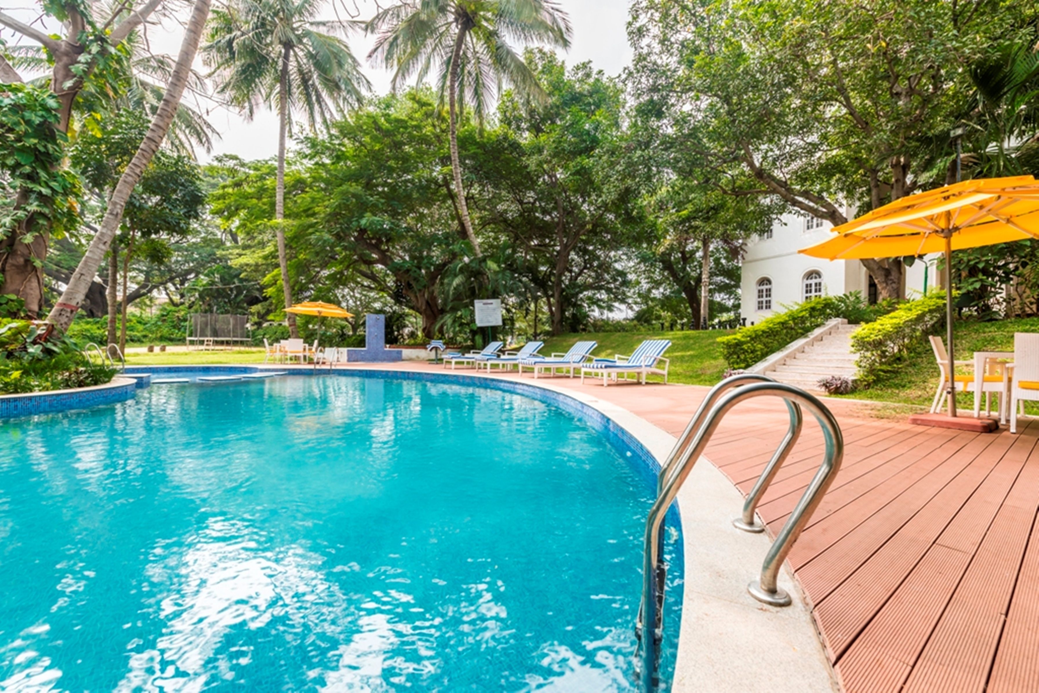 A swimming pool with a wooden deck, lounge chairs, and palm trees in the background.