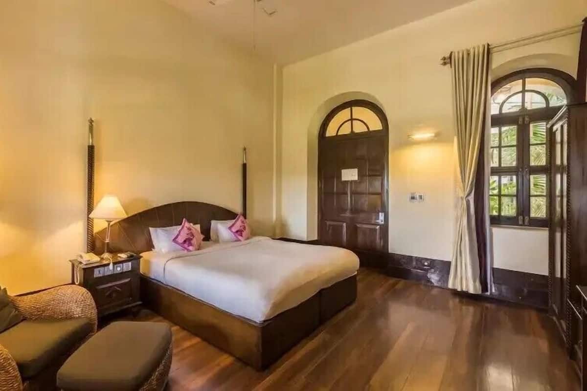 Quarto de hotel com cama, mesas de cabeceira, uma cadeira e uma janela com cortinas.