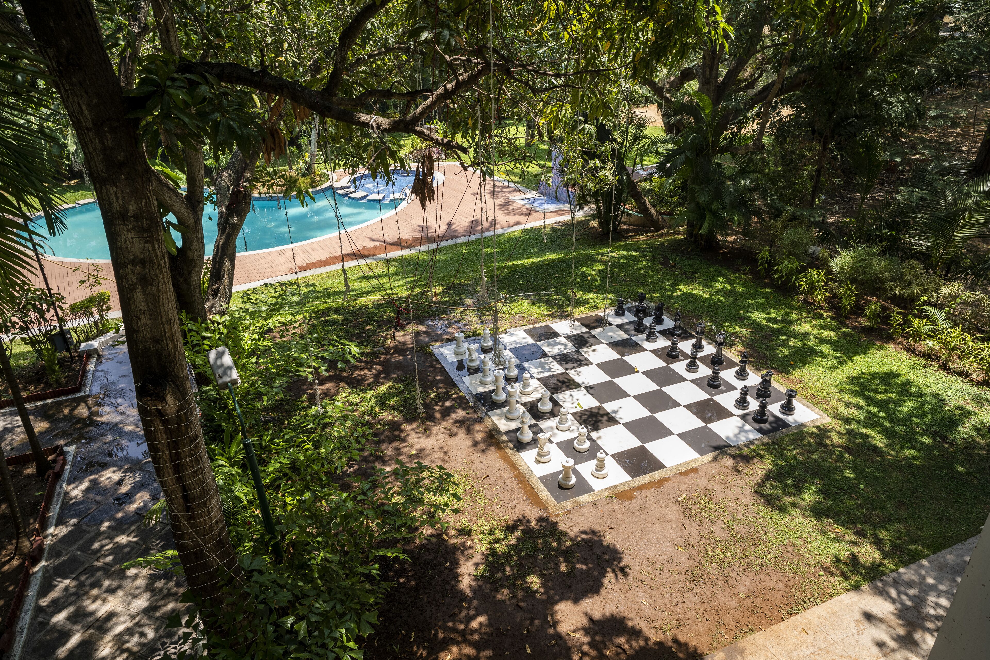 Zona de piscina con un tablero de ajedrez a cuadros y piezas, rodeada de abundante vegetación.