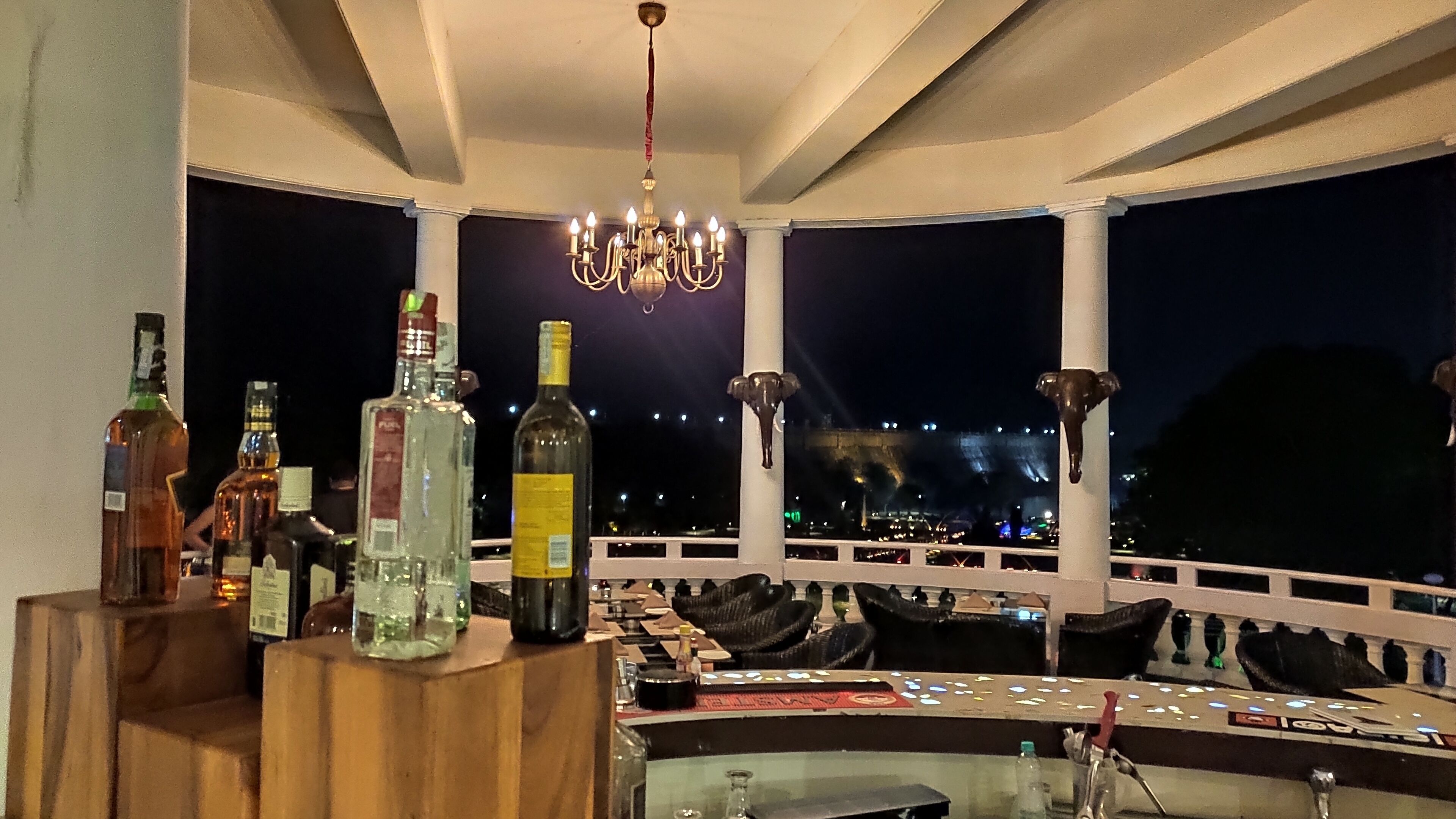 Eine Bar mit Flaschen und Gläsern, einer Kronleuchter und Blick auf eine nächtliche Skyline.
