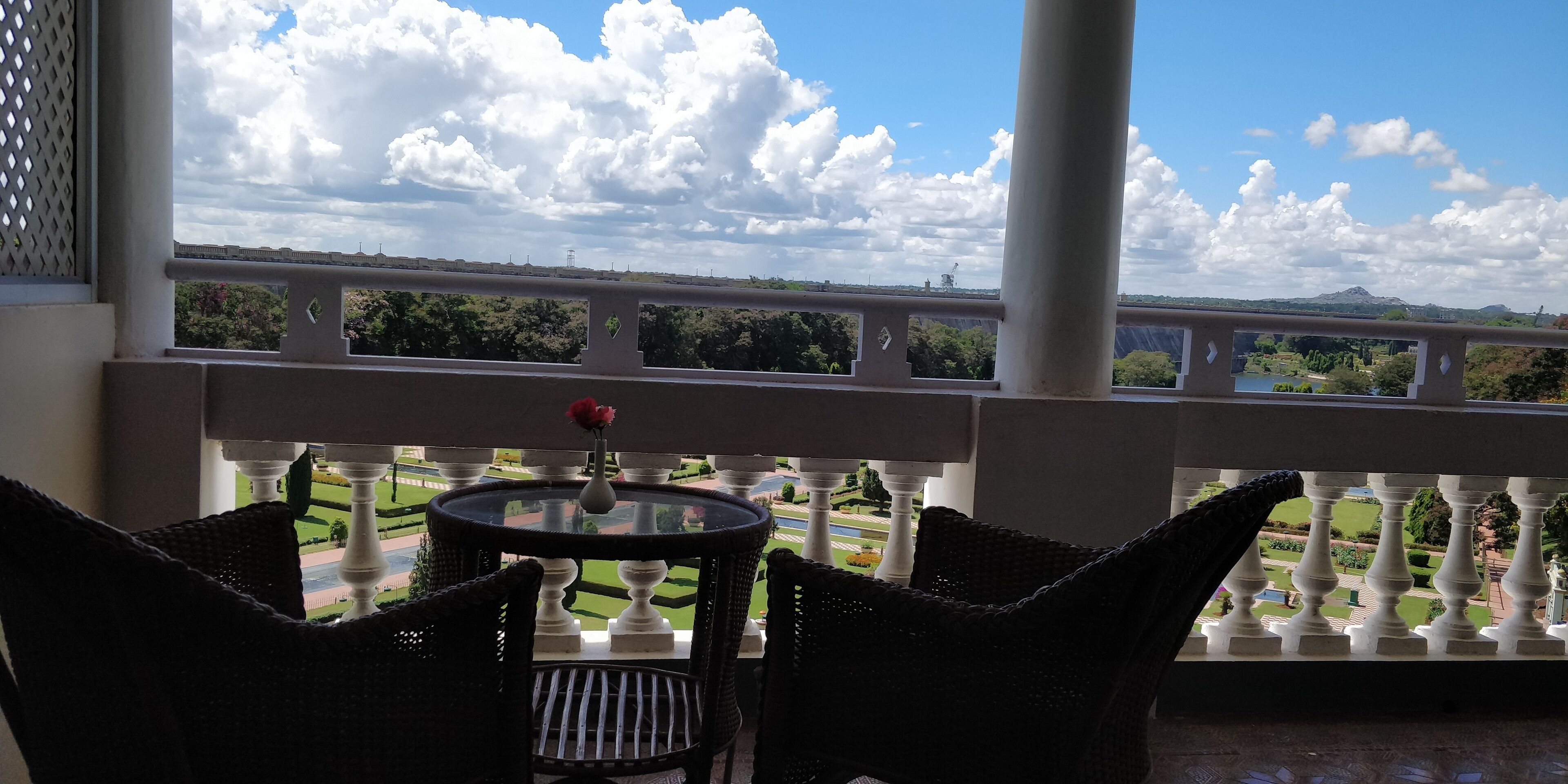 Ein Balkon mit Tisch und Stühlen, mit Blick auf einen angelegten Garten und eine entfernte Brücke.