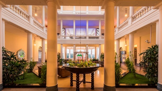 Un lobby amplio con techos altos, una mesa redonda central con plantas, y un balcón con vistas al espacio.