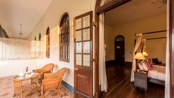 A room with a wooden door, wicker chairs, a small table with a teapot, and a lamp on a nightstand.