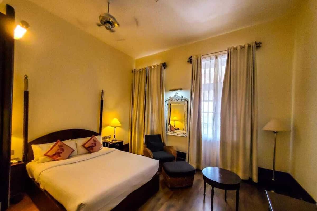 Quarto de hotel com uma cama grande, uma cadeira, uma mesinha e uma mesa de cabeceira com abajur.