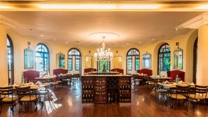 Un comedor amplio con varias mesas y sillas, un candelabro central y estanterías para vino.