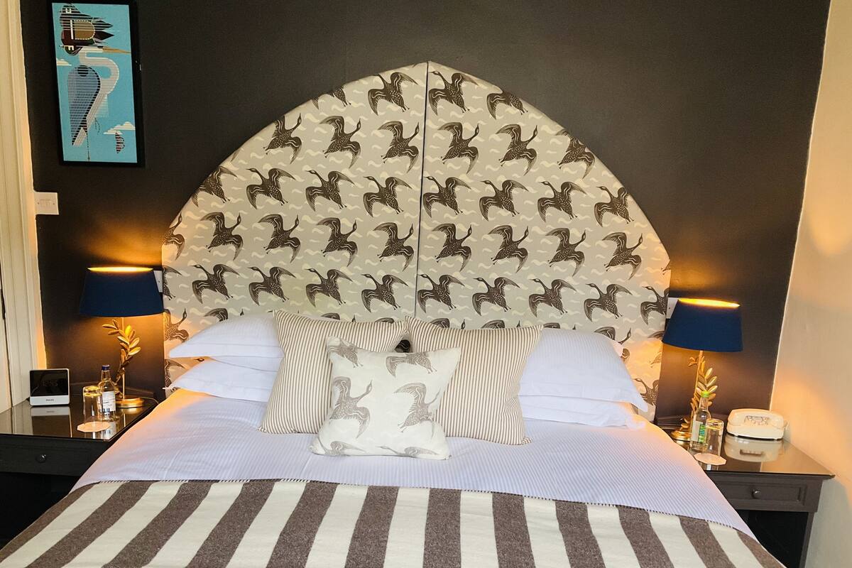 A hotel room with a large bed, striped bedding, a headboard with a bird pattern, two bedside tables with lamps, and a wall-mounted artwork.