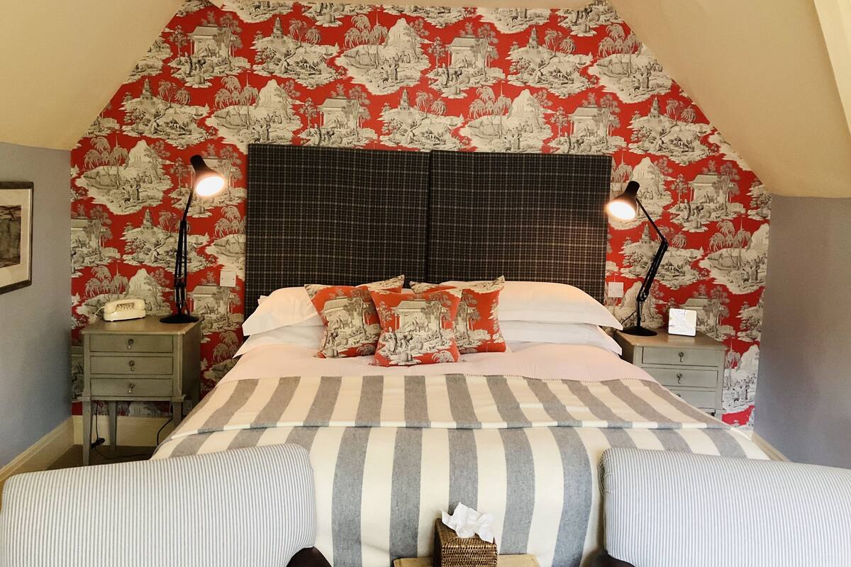 A bedroom with a bed, two bedside tables, a lamp, and a patterned wallpaper.