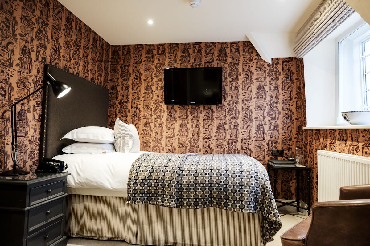 A bedroom with a bed, a bedside lamp, a television on the wall, and a radiator.
