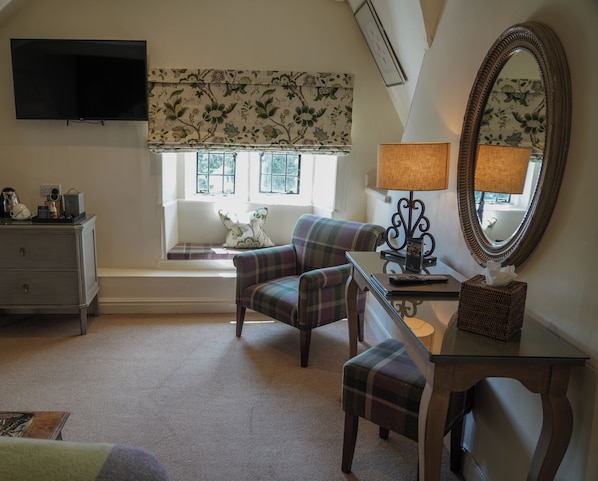 A cozy room with a plaid armchair, a small table with a lamp, a dresser, and a large mirror. - The Close Hotel (Tetbury)
