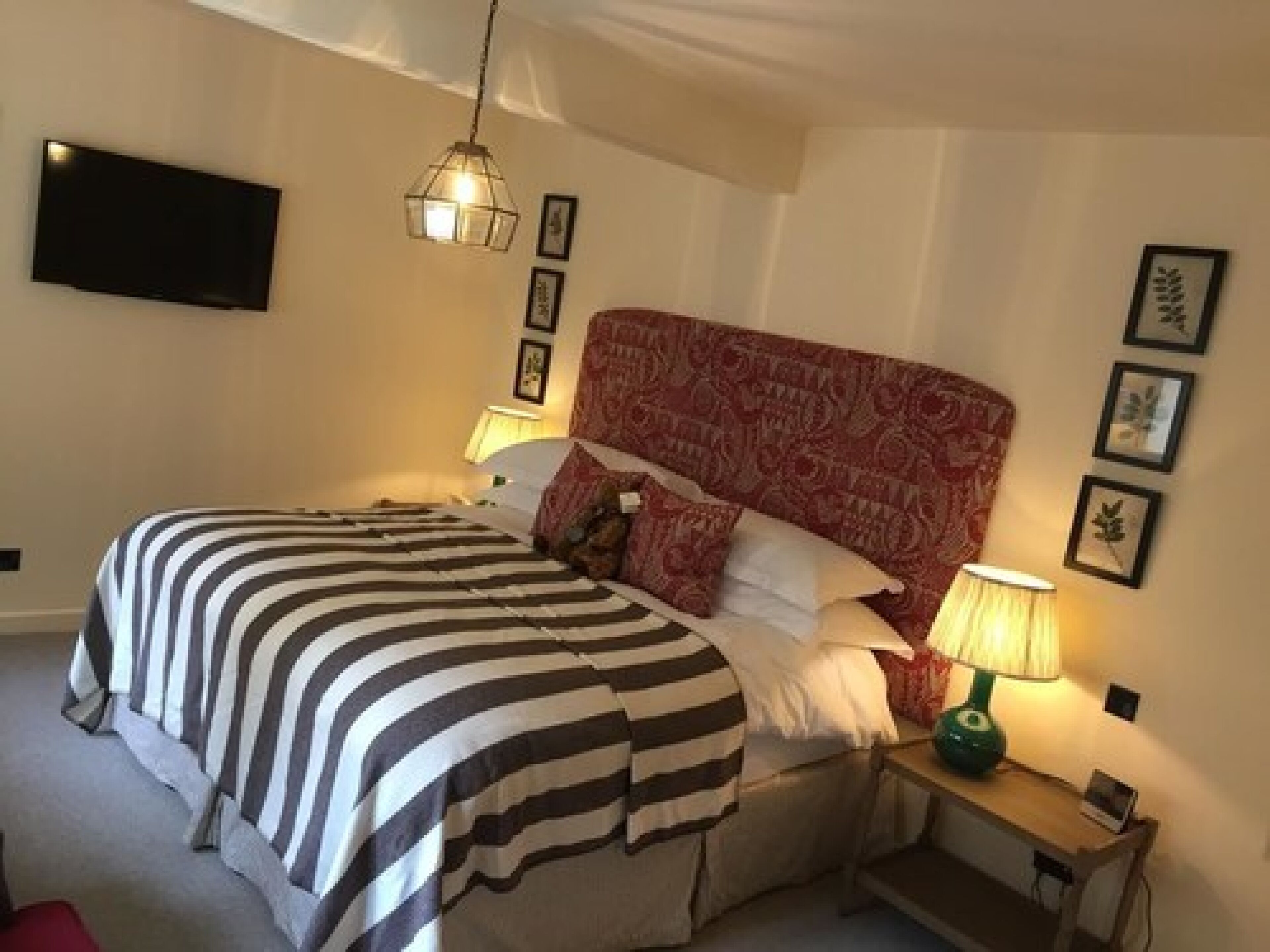A hotel room with a large bed, a bedside table with a lamp, and a TV mounted on the wall.