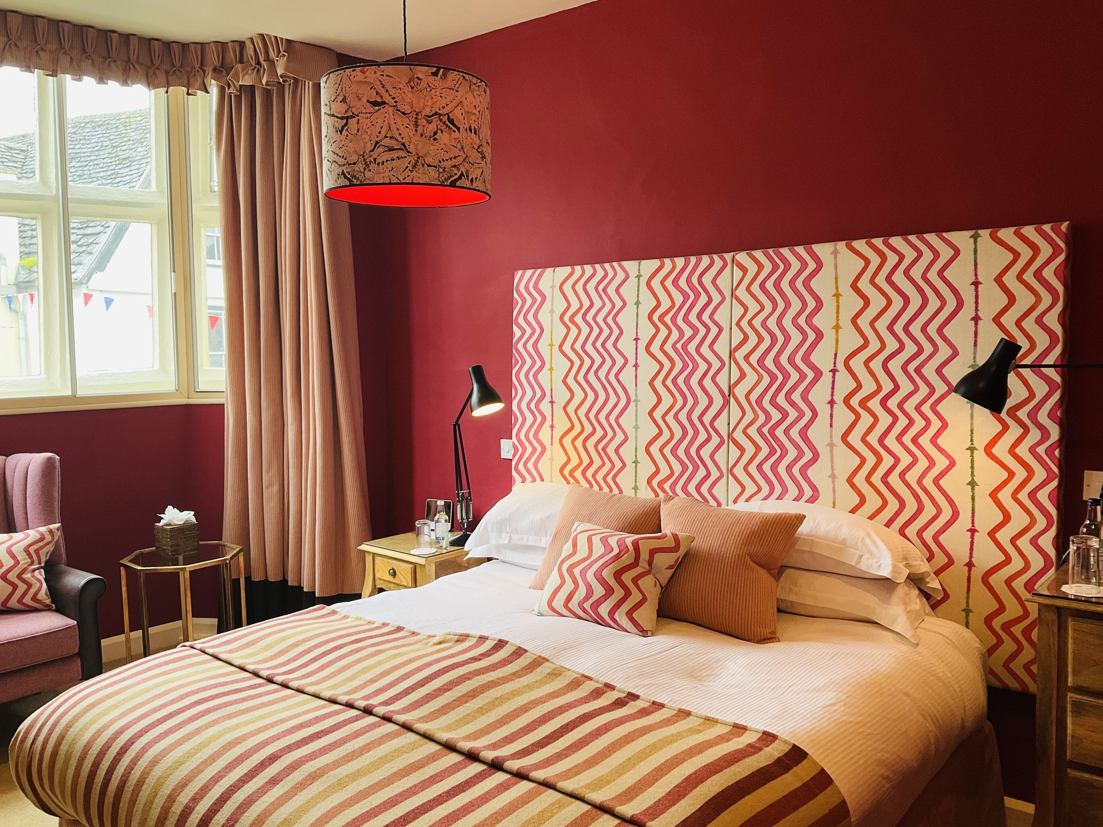 A hotel room with a large bed, a bedside table with a lamp, a chair, and a window with curtains.