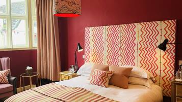 A hotel room with a large bed, a bedside table with a lamp, a chair, and a window with curtains.