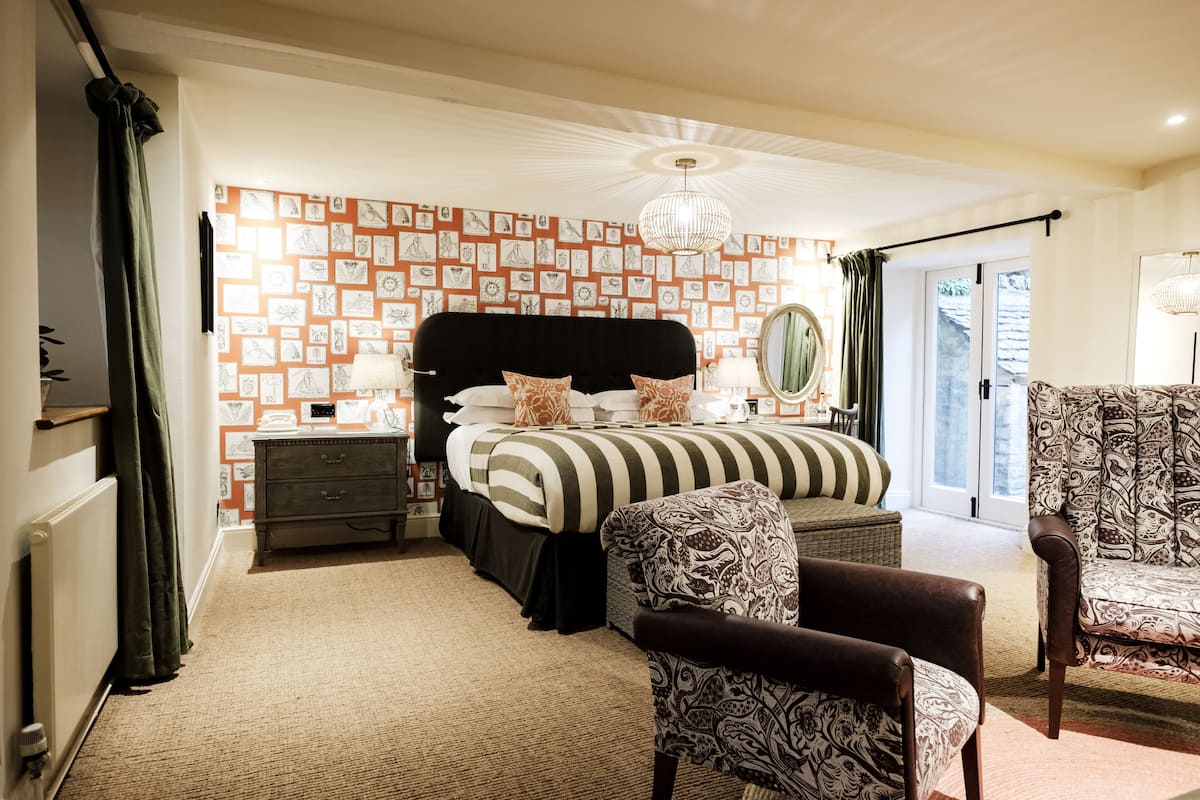 A bedroom with a bed, a dresser, a chair, a patterned wall, and a chandelier.