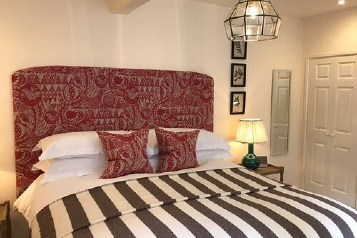 A hotel room with a patterned headboard, a striped bedspread, a bedside lamp, and framed pictures on the wall.