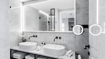 Une salle de bain moderne avec deux vasques blanches, un grand miroir et une douche.