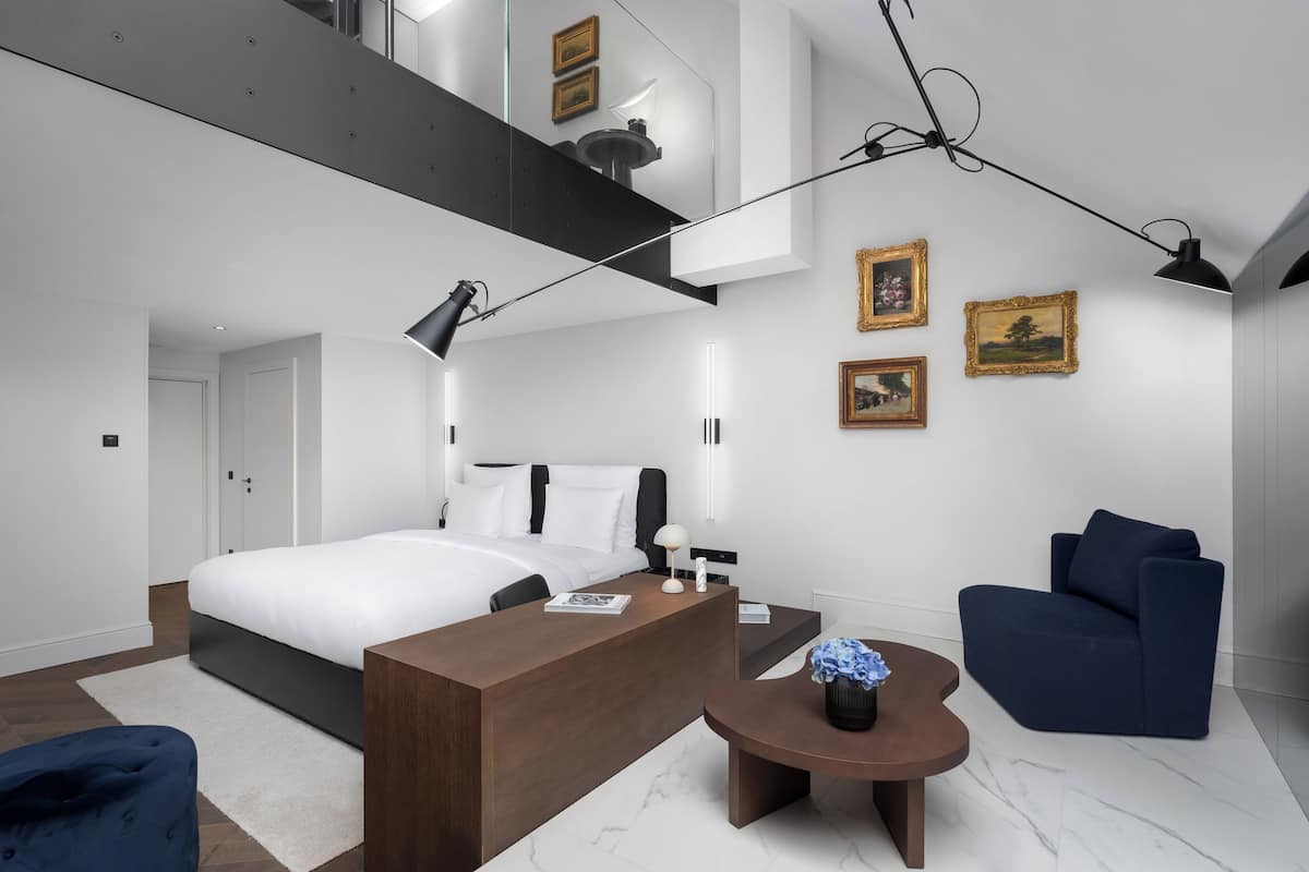 A modern bedroom with a large bed, a desk, a chair, and a small table with a vase.