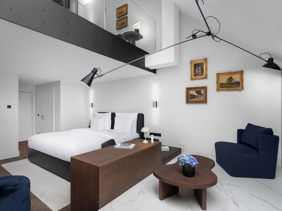 Un dormitorio moderno con una cama grande, un escritorio, una silla y una mesita con un florero.