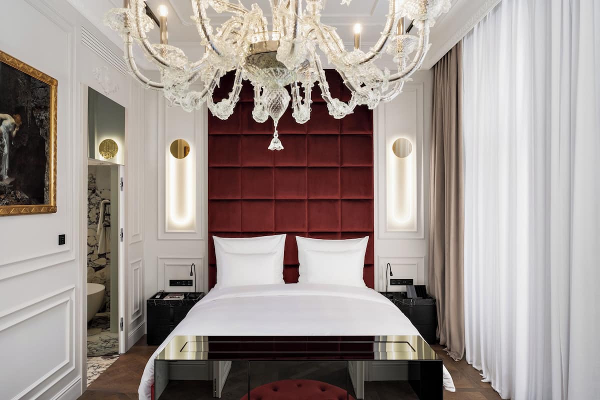 A luxurious bedroom with a large bed, a red upholstered headboard, a chandelier, and a painting on the wall.