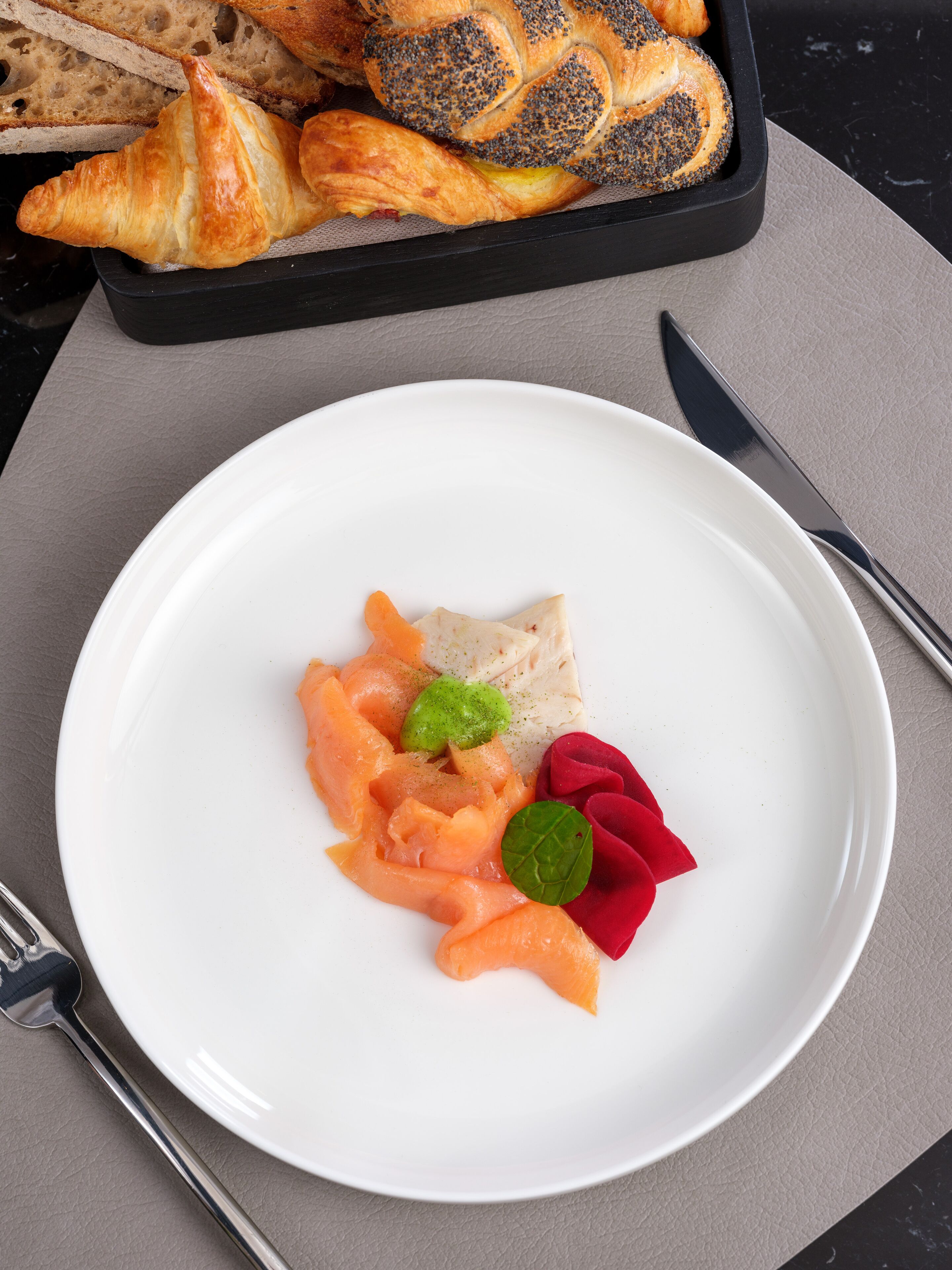 A white plate with salmon, beets, and a green leaf garnish.