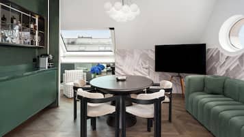 A modern living room with a round dining table, a green sofa, a TV, and a window with a view of buildings.