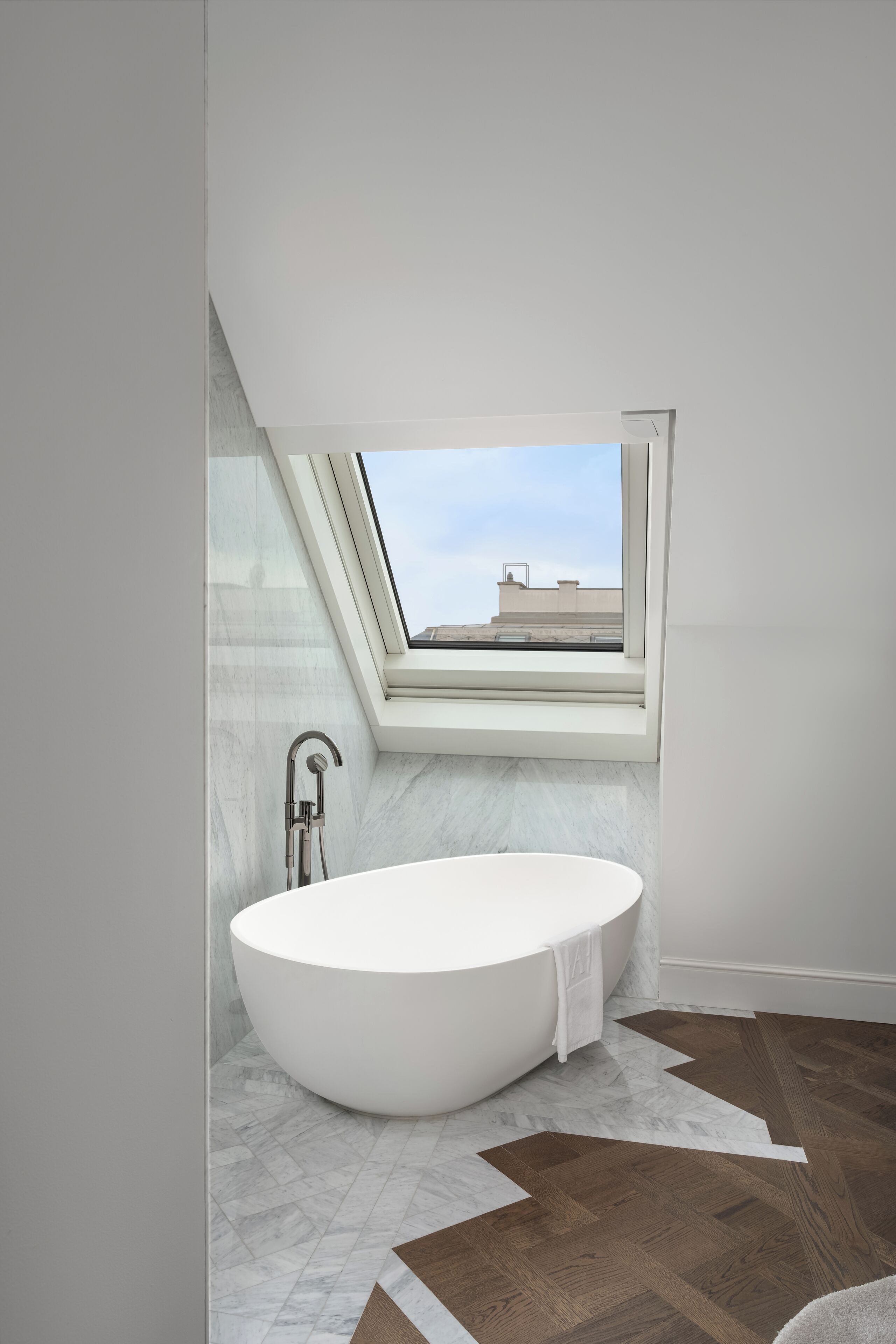 A modern bathroom with a freestanding bathtub, a skylight, and a view of the cityscape.