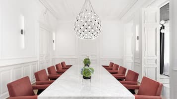 A conference room with a marble table, red chairs, a decorative hanging light, and white walls.