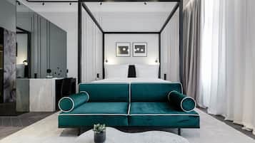 A modern hotel room with a large bed, a green sofa, a marble coffee table, and a small plant.
