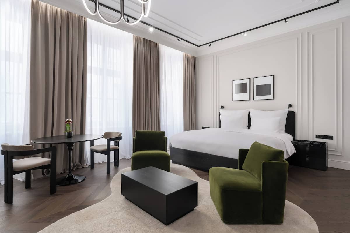 A modern hotel room with a large bed, two chairs, a small table, and a coffee table.