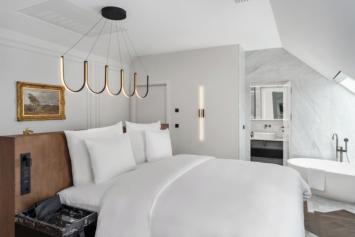 A modern hotel room with a large bed, a built-in desk, a bathroom with a bathtub, and a skylight.