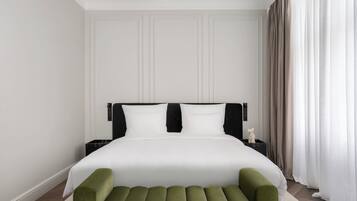 A modern hotel room with a large bed, a green bench, and a nightstand with a lamp.