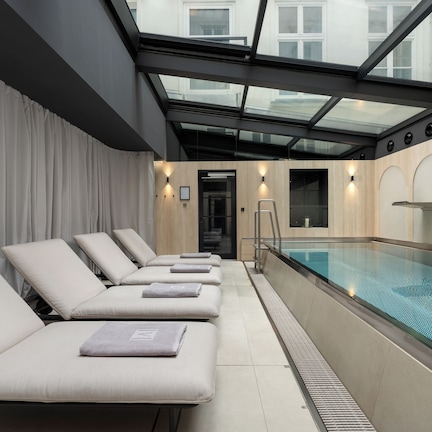 A modern indoor pool area with a glass ceiling, multiple lounge chairs, and a clear view of the pool.