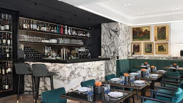 A restaurant with marble walls, a bar area with shelves of bottles, and green upholstered seating.