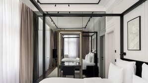 Een moderne hotelkamer met een groot bed, een bureau en een stoel. Er hangt een spiegel aan de muur en er is een raam met gordijnen.