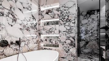 Une salle de bain moderne avec une grande baignoire ovale, des murs en marbre et une douche séparée par des parois en verre.