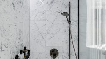 A modern bathroom with a shower, a glass-enclosed corner, and a shelf with toiletries.