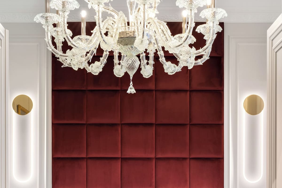 A luxurious bedroom with a large mirror, a red upholstered headboard, and a chandelier.