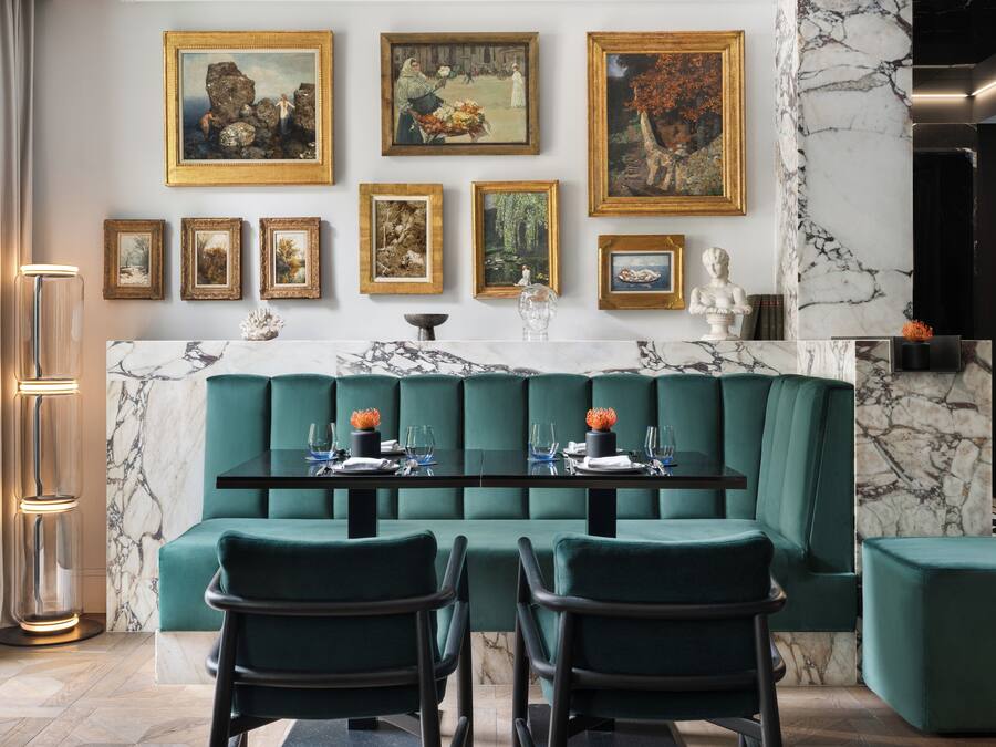 Un comedor con encimera de mármol, asientos tapizados en verde y obras de arte enmarcadas en la pared.